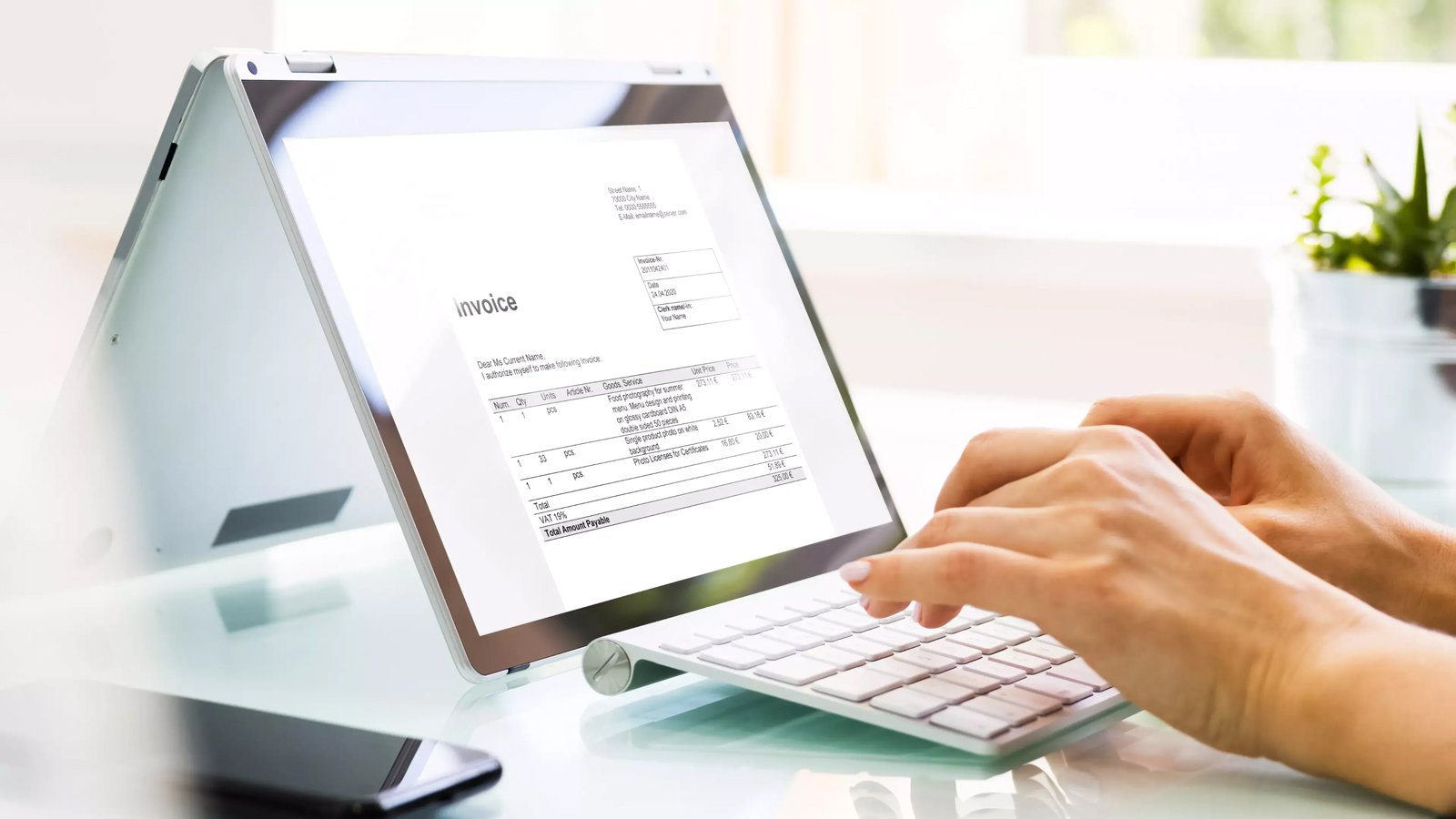 Person types on a keyboard while an invoice is visible on a screen in tent mode, as part of a cash application process.