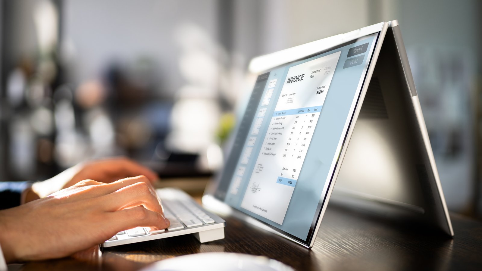 Persoon typt op toetsenbord terwijl een e-invoicing factuurscherm zichtbaar is op een laptop in tentstand op een bureau.