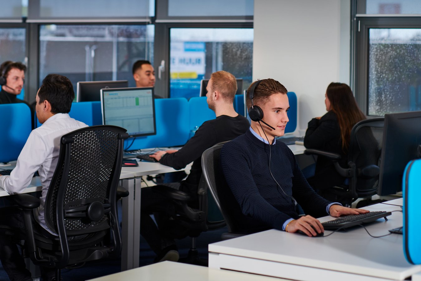 Debt Collection. Employees with headsets at work in a modern office with separate workstations and computer screens