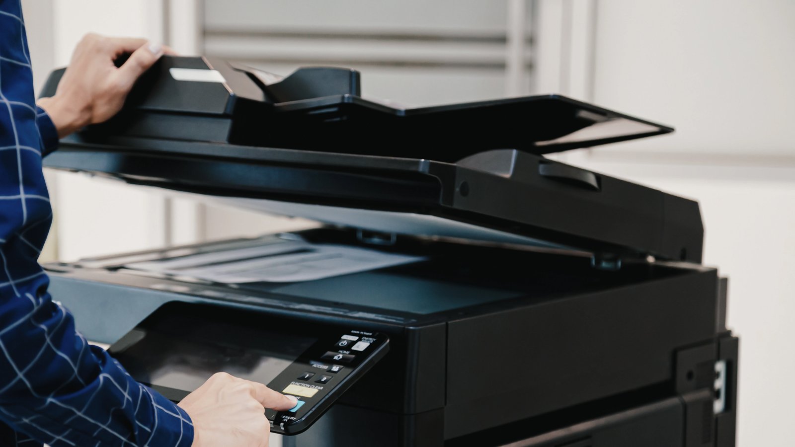 Handen die een printer bedienen met op de achtergrond een scherm, symbool voor digitale verwerking van print en post diensten.