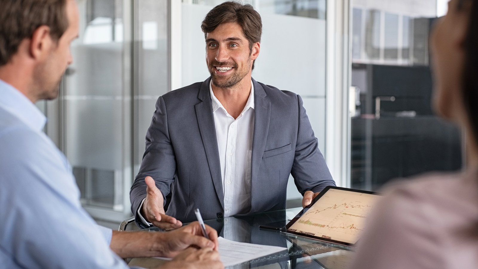 Zakelijke bespreking tussen drie mensen waarbij een adviseur op een tablet grafieken toont over financieringsopties binnen de financial marketplace